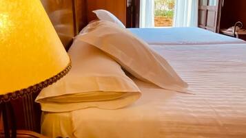 A hotel room with a bed, a desk with a lamp, and an open window.