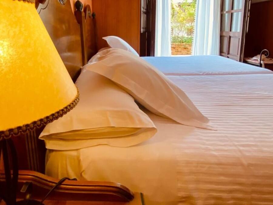 A hotel room with a bed, a desk with a lamp, and an open window.