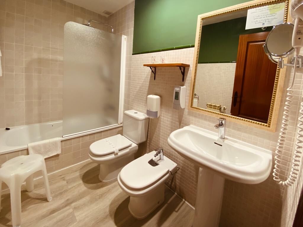 A bathroom with a bathtub, two toilets, a sink, and a mirror.