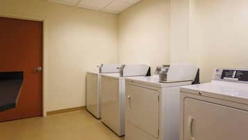 Una sala de lavandería con cuatro lavadoras y secadoras de carga frontal, una puerta de madera y piso de baldosas.
