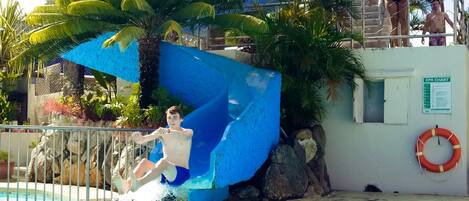 A pool with a blue slide and palm trees.