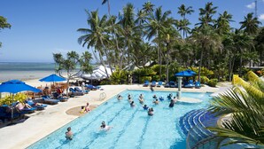A pool area with lounge chairs and umbrellas, surrounded by palm trees and a view of the ocean. - Fiji Hideaway Resort and Spa (Korolevu)