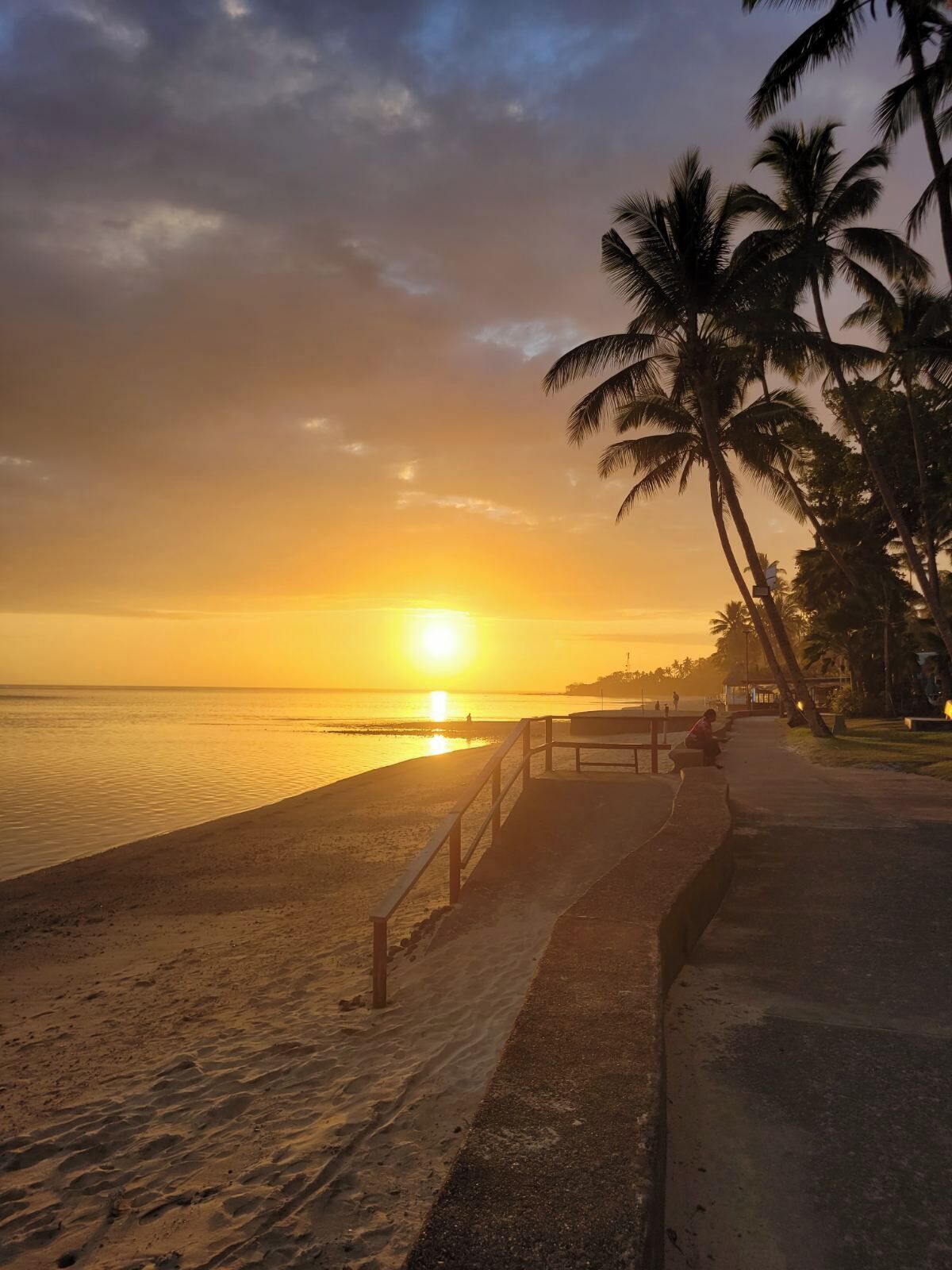 A sunset beach scene with a walkway and palm trees.