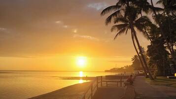 A sunset beach scene with a walkway and palm trees.