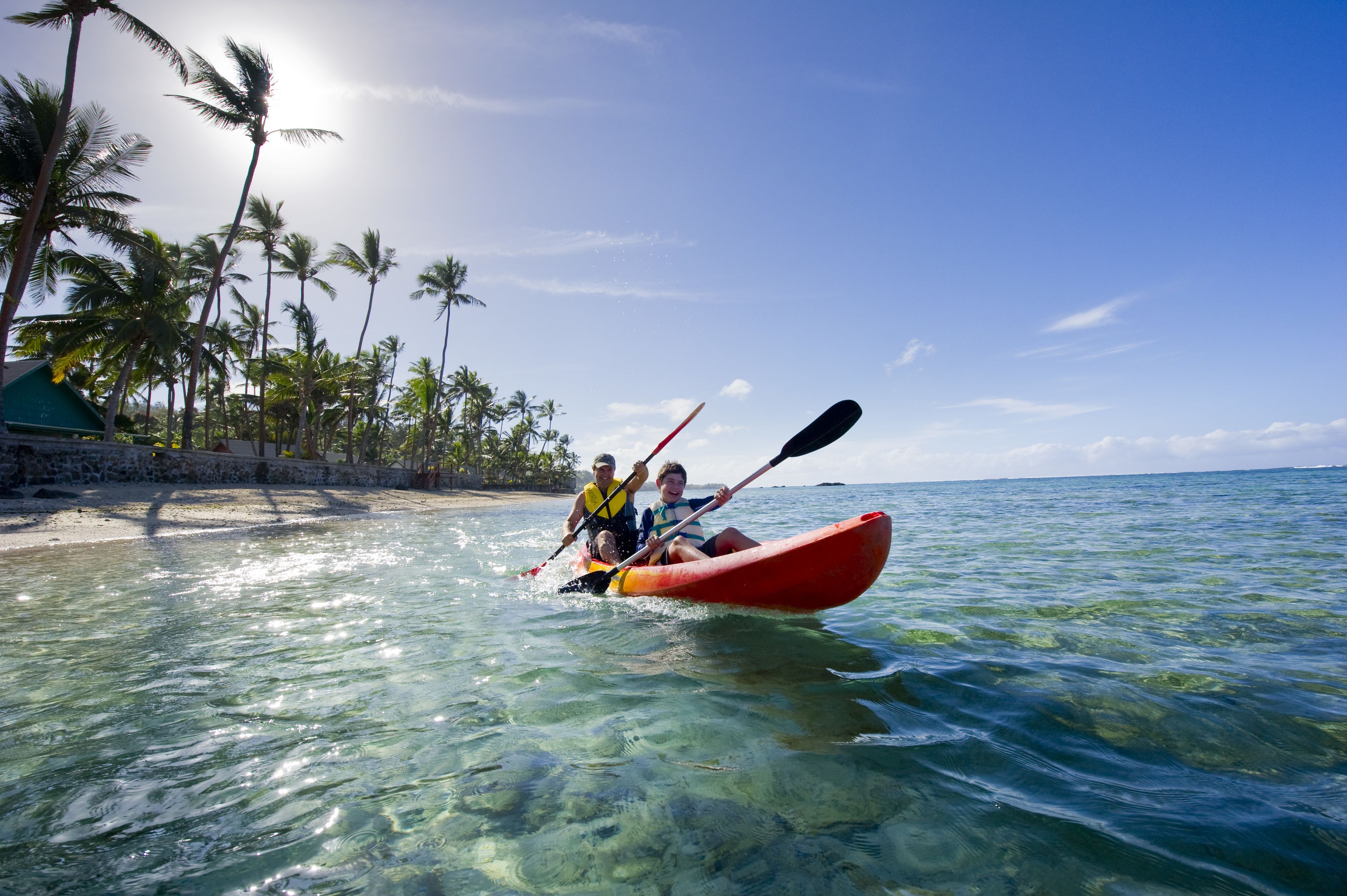 A kayak on clear turquoise water with palm trees and a beach in the background.