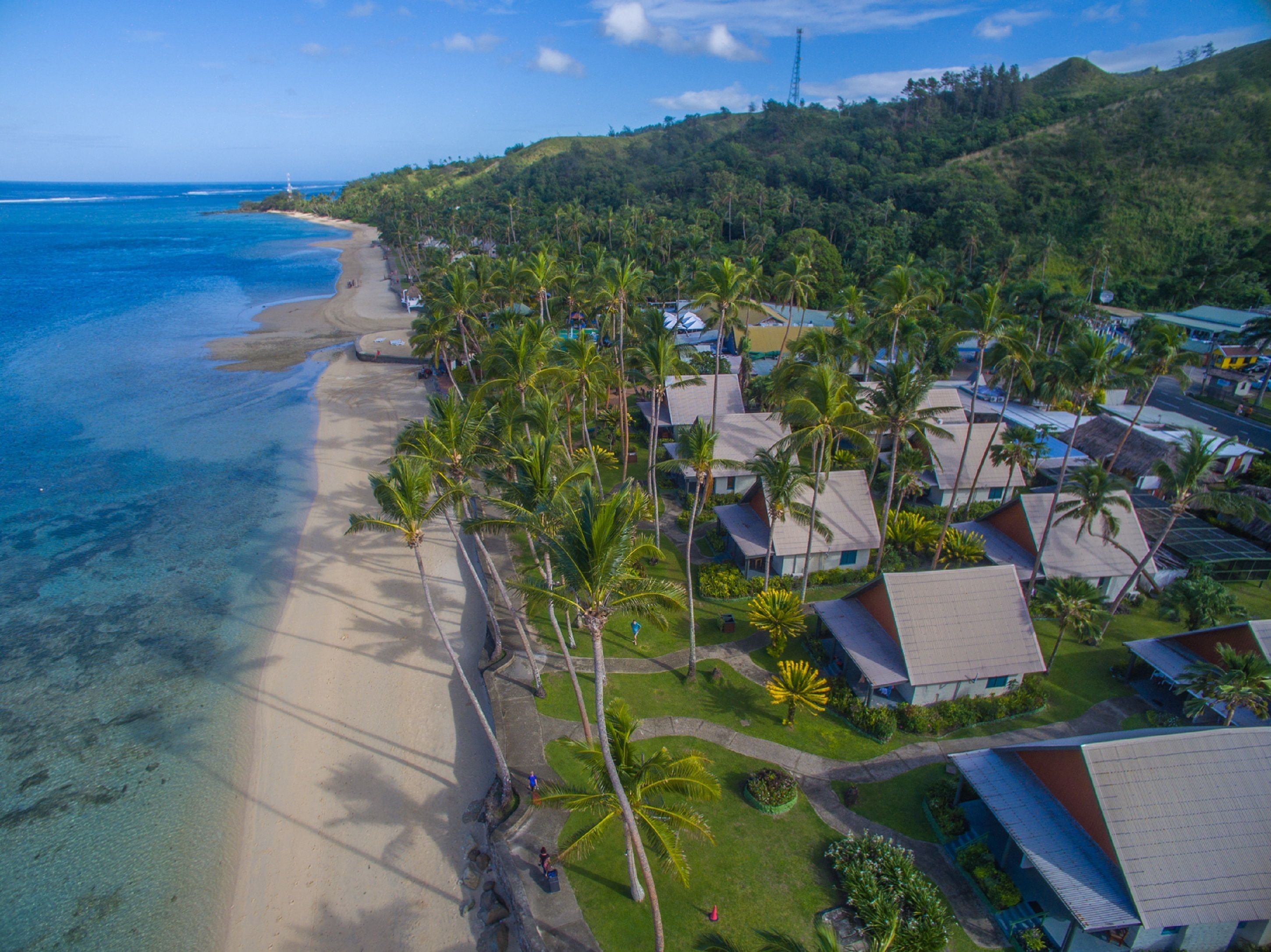 Eine Luftaufnahme eines Küstenresorts mit Strandvillen, Palmen und freiem Blick auf den Ozean.
