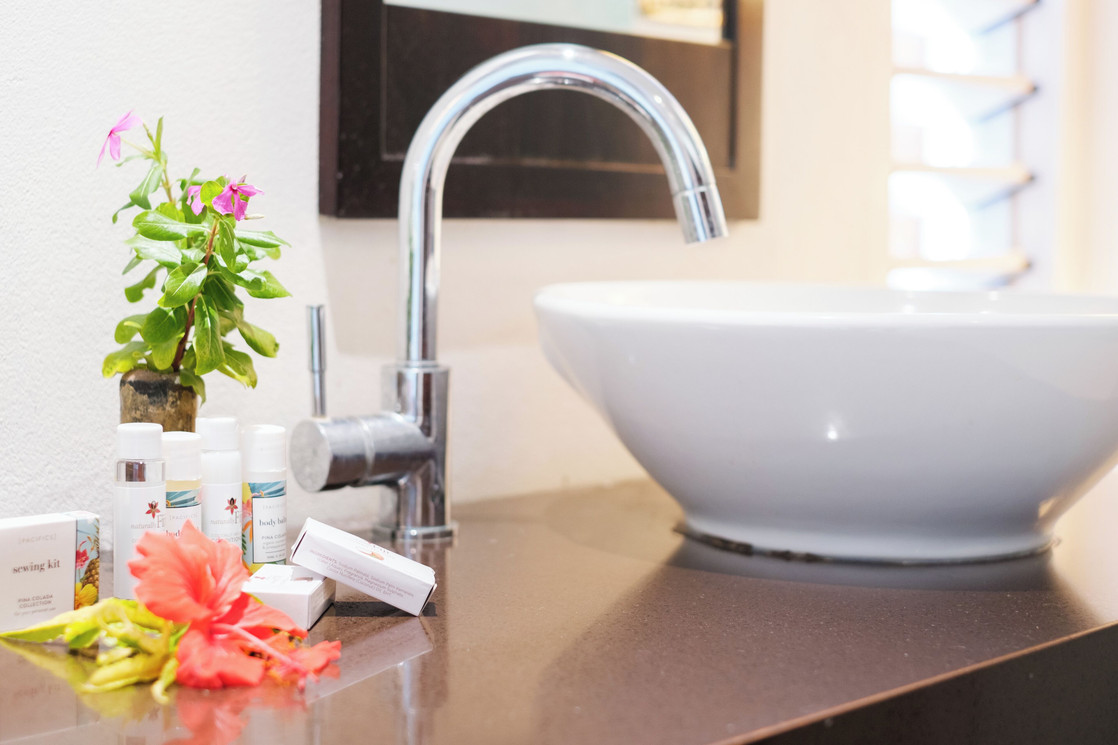 Uma pia de banheiro com uma torneira moderna, uma cuba branca e um pequeno vaso com flores cor-de-rosa.