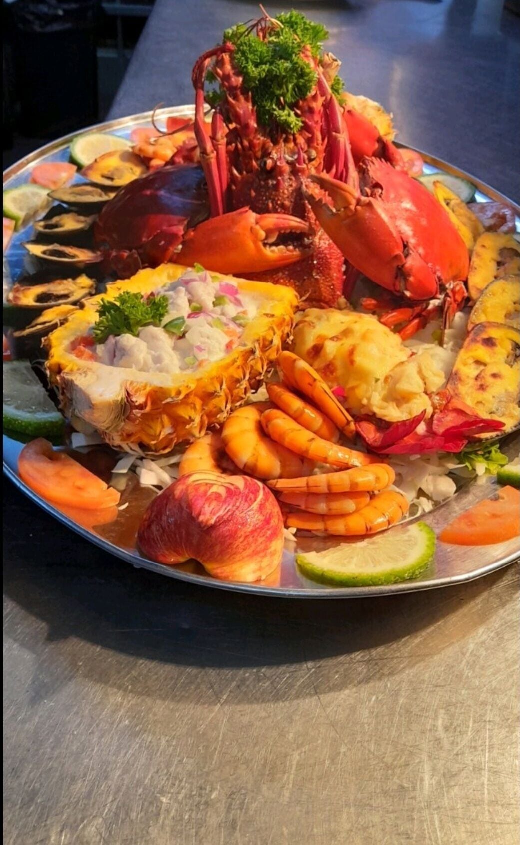 A seafood platter with various shellfish, including a lobster, shrimp, and crab, along with sliced vegetables and a garnish of parsley.