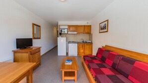 A compact room with a wooden table, a television, a kitchenette, and a sofa with a red and brown checkered cover. - Noemys les Toits du Devoluy (Le Dévoluy)