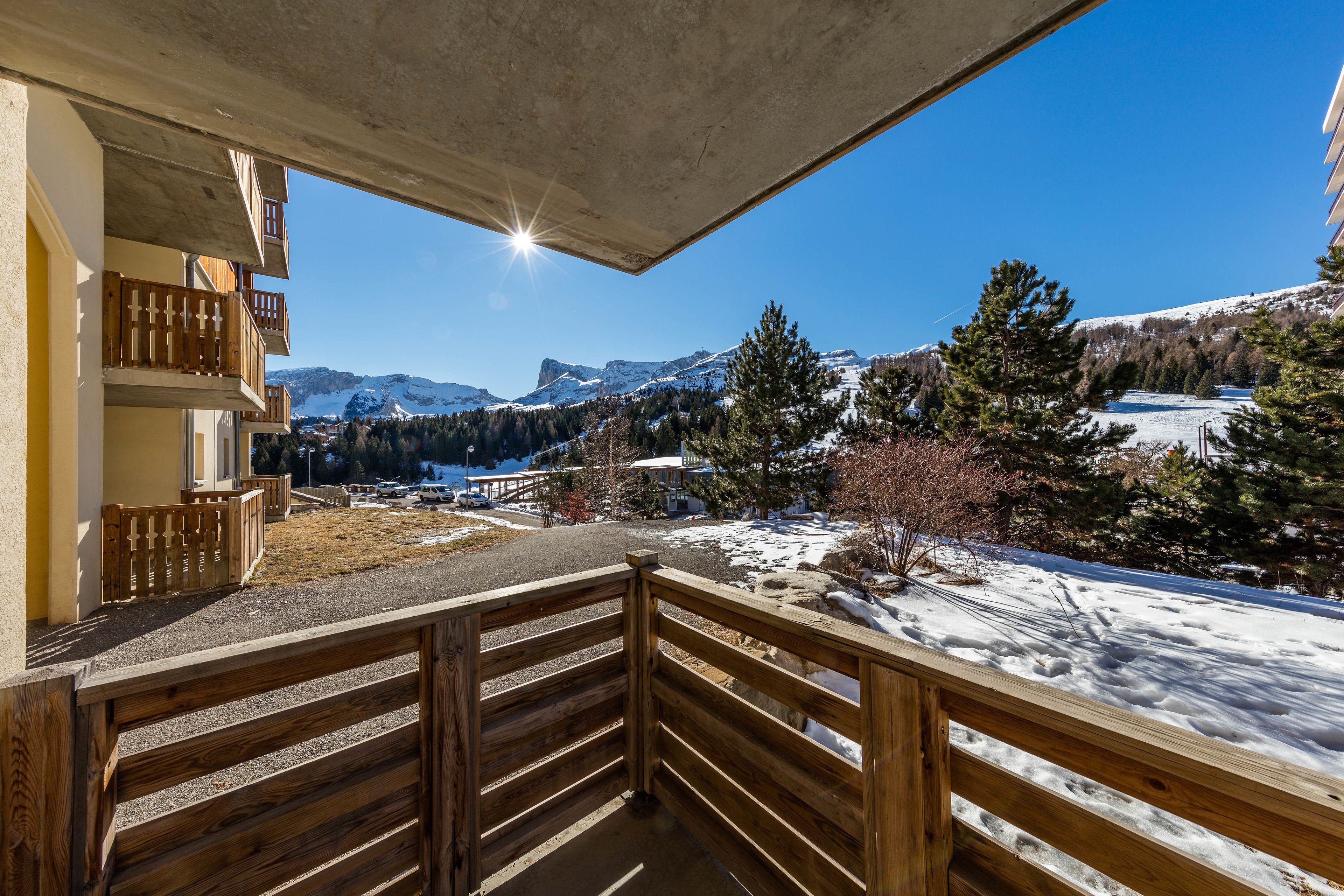 Un balcon en bois offrant une vue sur des montagnes enneigées et un ciel bleu dégagé.