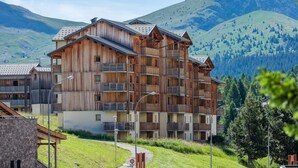 A multi-story wooden building with balconies, set against a mountainous backdrop. - Noemys les Toits du Devoluy (Le Dévoluy)