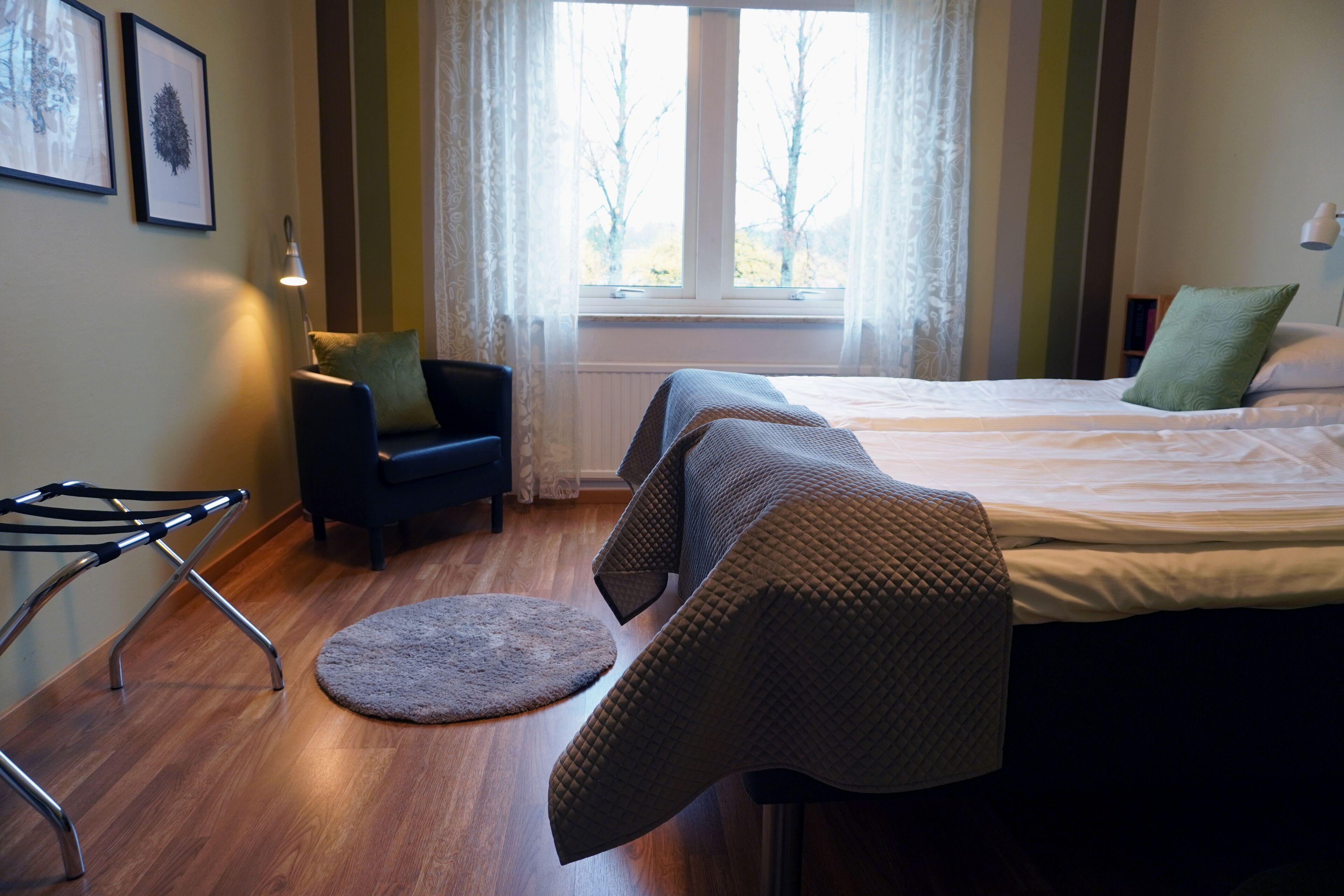 Una habitación de hotel con cama, una silla, una mesita y una ventana con cortinas.