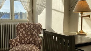 A room with a patterned armchair, a wooden dining table, a lamp, and a window with sheer curtains. - Stjärnholms slott (Oxelosund)