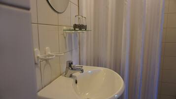 A bathroom with a white sink, a mirror, and a glass shelf with decorative items.