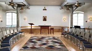 A spacious hall with wooden floors, a patterned rug, and rows of chairs. - Stjärnholms slott (Oxelosund)