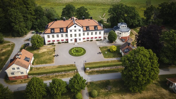 A large, white building with a red-tiled roof, surrounded by a well-maintained lawn and a lake. - Stjärnholms slott (Oxelosund)