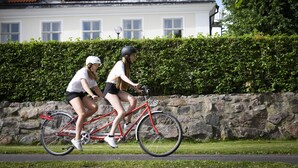 Two people riding a red bicycle on a paved path next to a stone wall and a hedge. - Stjärnholms slott (Oxelosund)