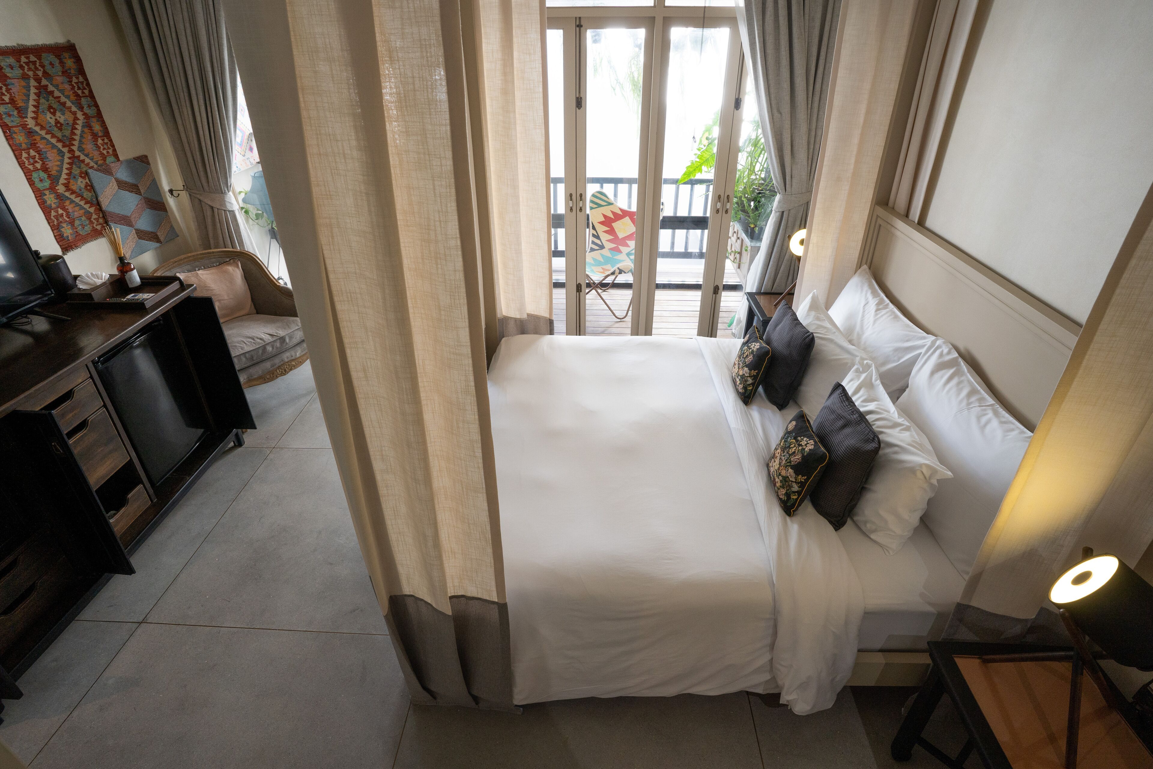 A hotel room with a bed, a desk with a computer, a chair, and a view of the outside balcony.
