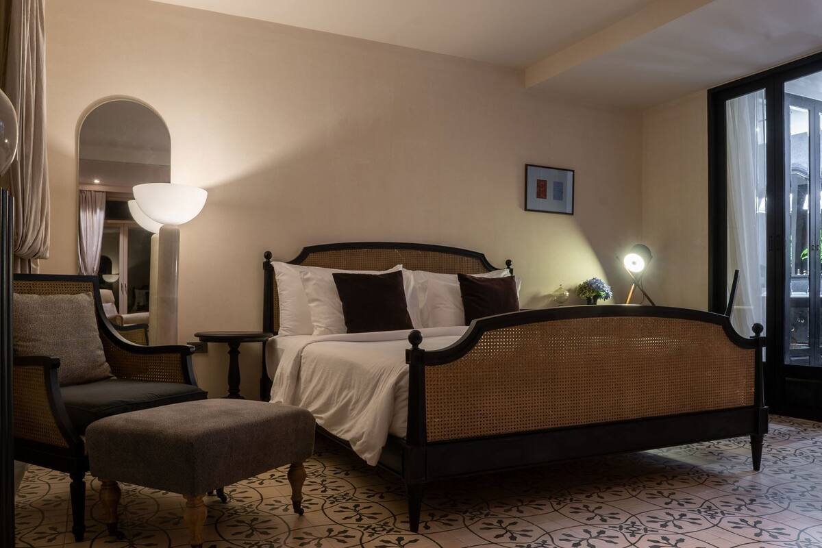 Un dormitorio con cama, una silla, una lámpara y vistas por la ventana.