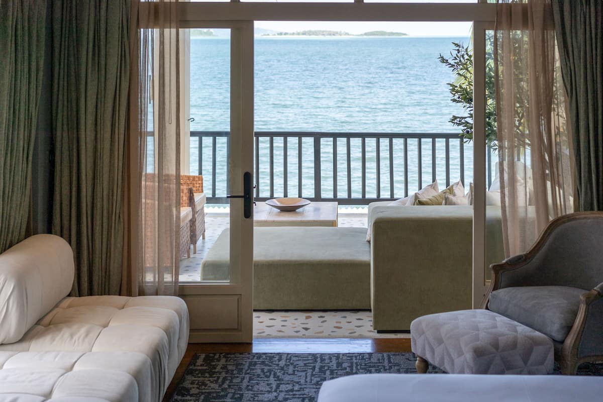 Una habitación con cama, una silla y vista al mar por medio de un ventanal.