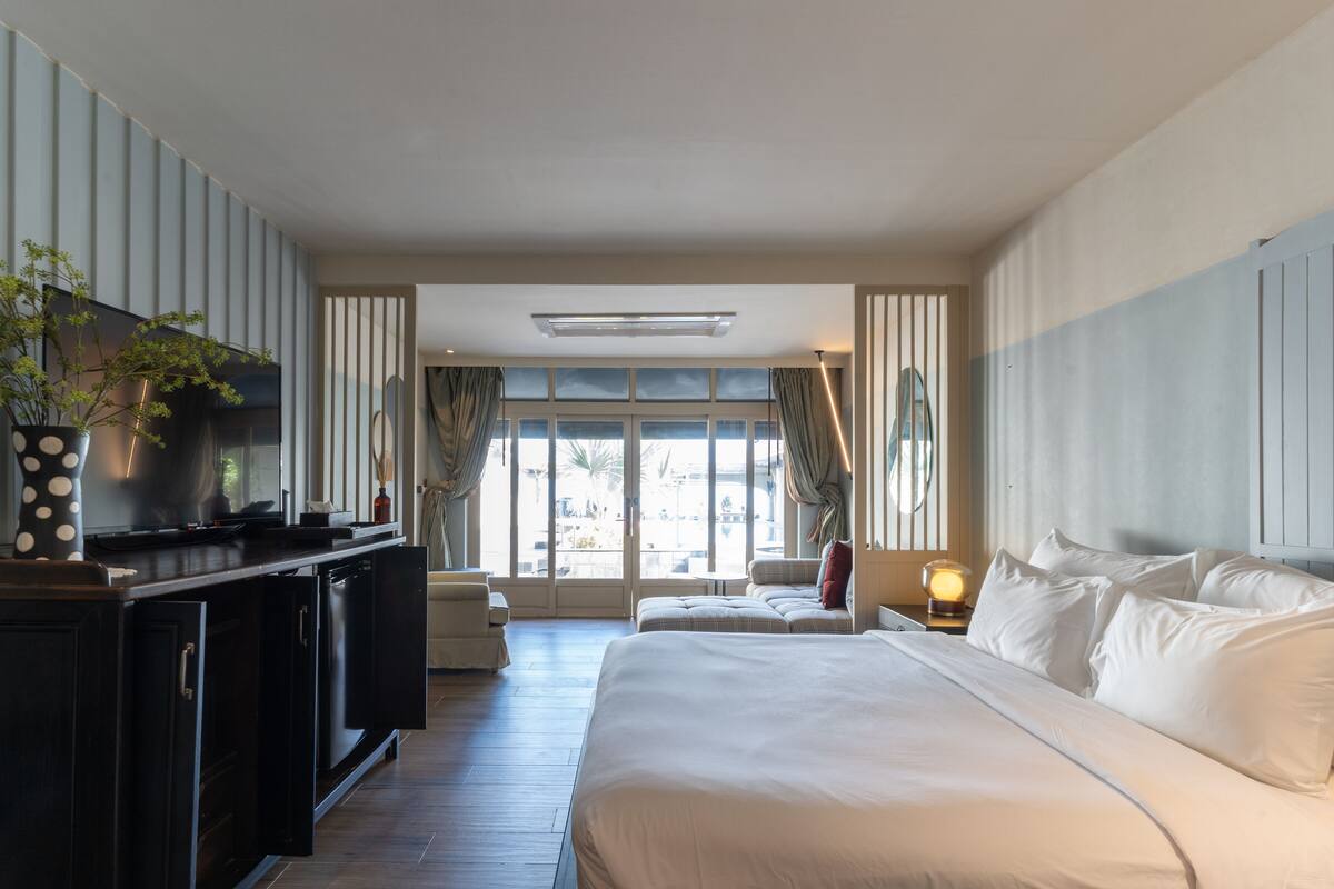 Una habitación de hotel con una cama grande, un escritorio con computadora, televisor y una ventana con cortinas.