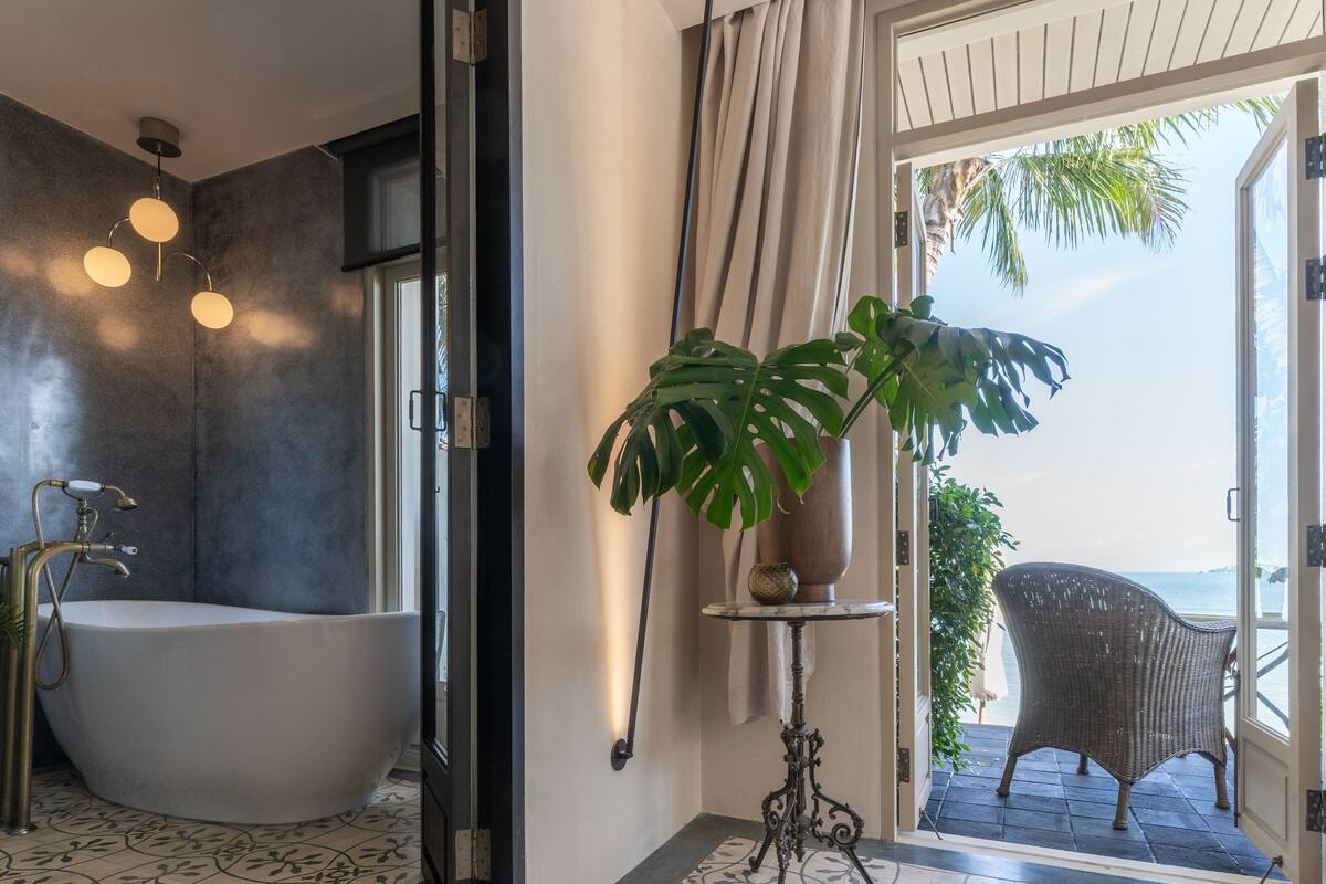 Un baño moderno con una bañera independiente, una planta en maceta y vistas al océano a través de un ventanal.