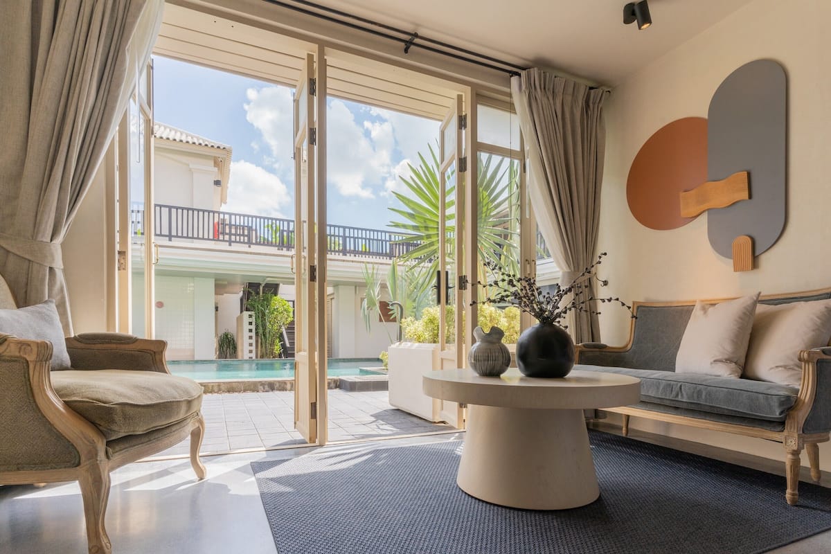 Una sala de estar moderna con un sofá, un sillón y una mesa de centro. Se ve un balcón con piscina a través de las puertas abiertas.