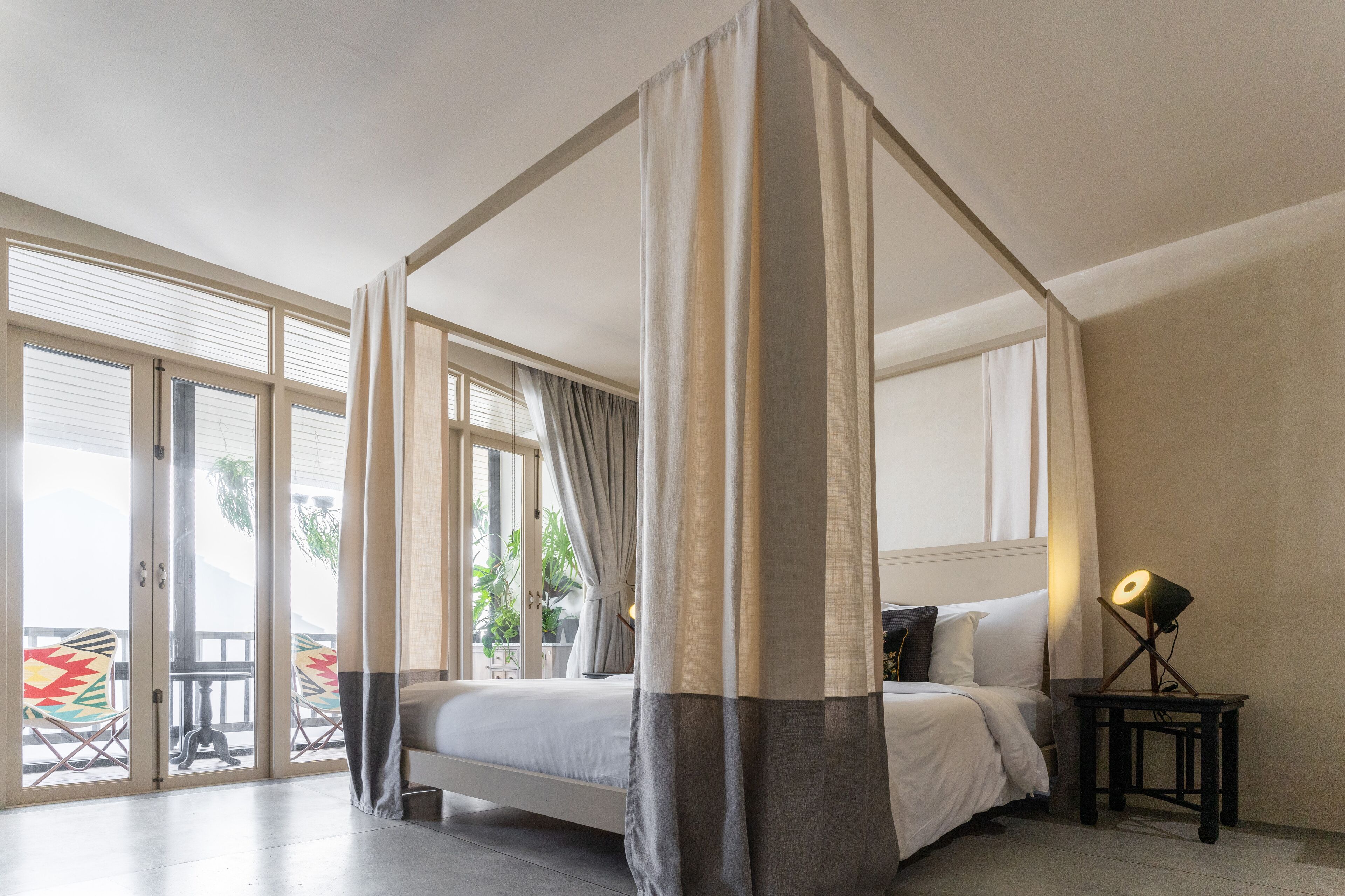 A bedroom with a four-poster bed, a nightstand with a lamp, and a view of the outdoors through large sliding doors.