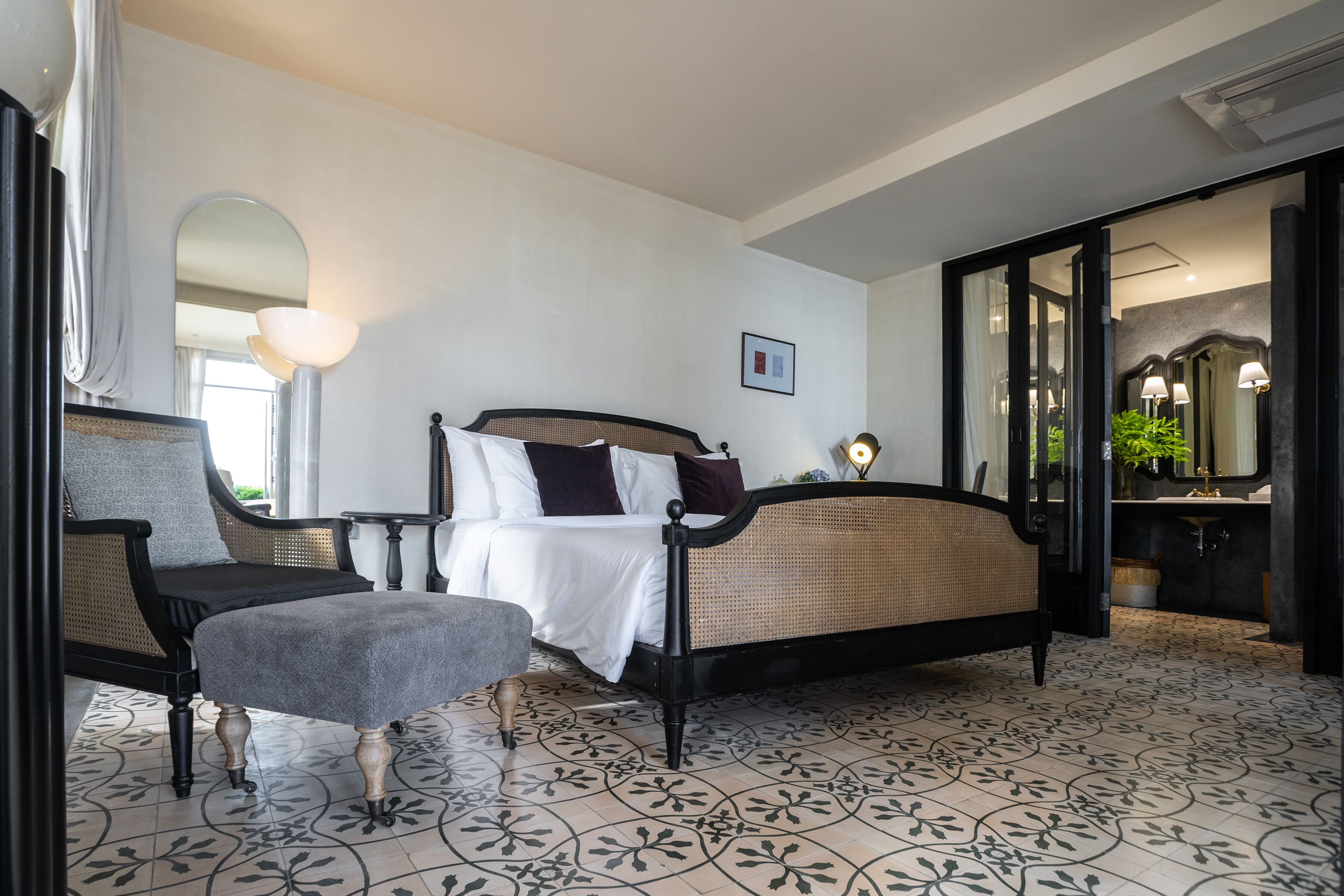 Un dormitorio con cama, una silla, una mesita y un espejo.