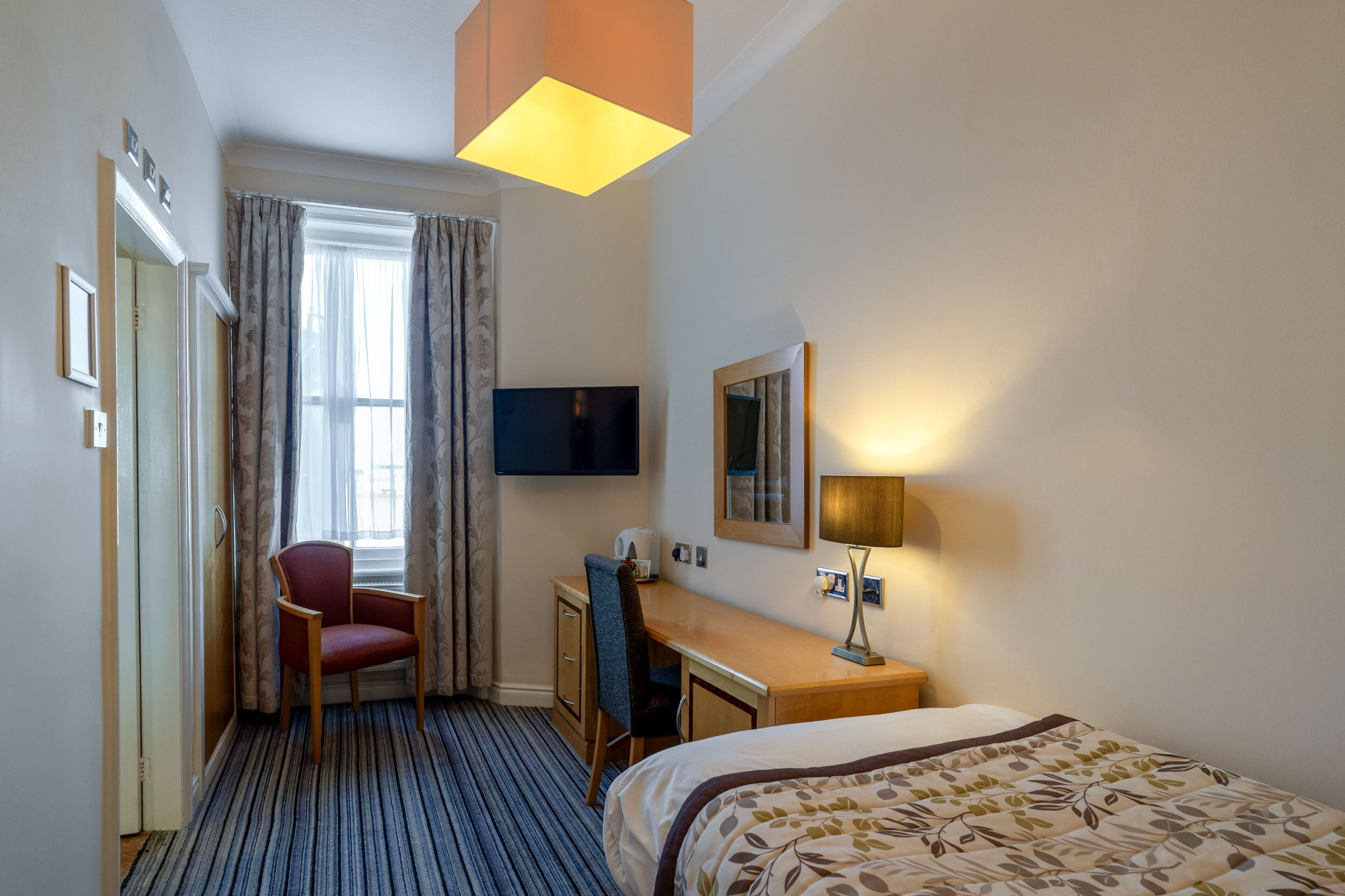A hotel room with a bed, a desk, a chair, a TV, and a window with curtains.