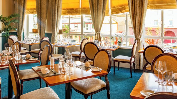 Un restaurante con varias mesas dispuestas para comer, sillas y vista a la calle.