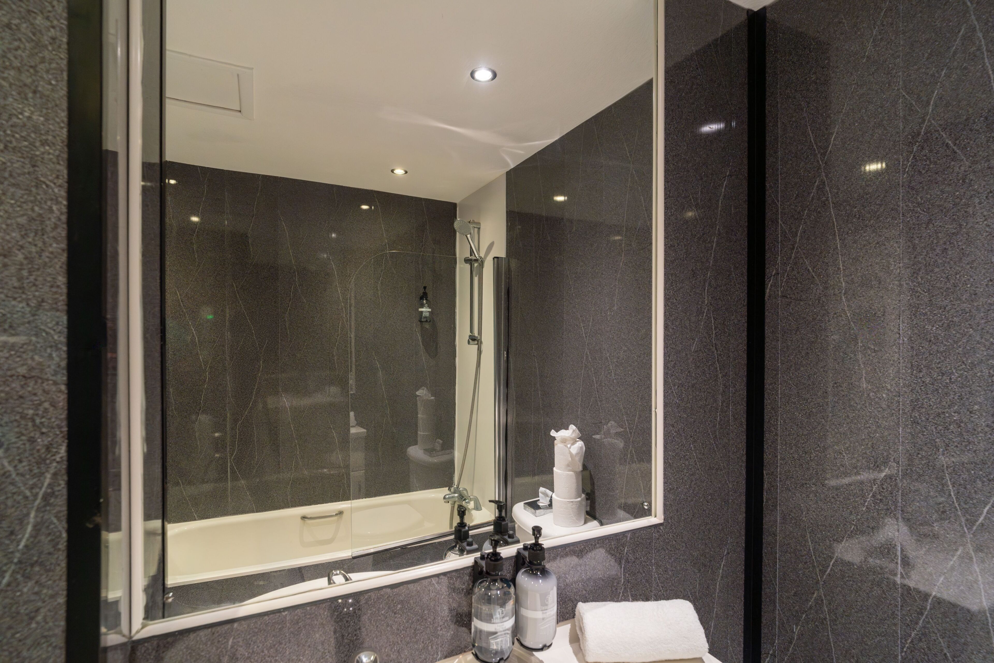 A modern bathroom with a large mirror, a shower, and a sink.