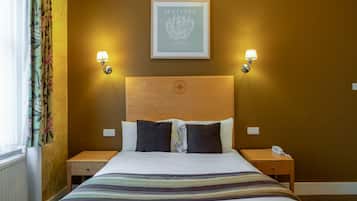 A hotel room with a bed, two bedside tables, a framed artwork on the wall, and a window with curtains.