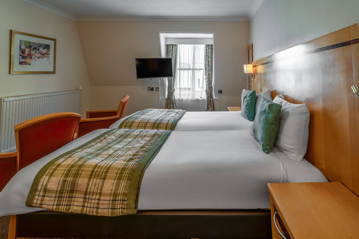 A hotel room with two beds, a television, a window with curtains, and a framed picture on the wall.