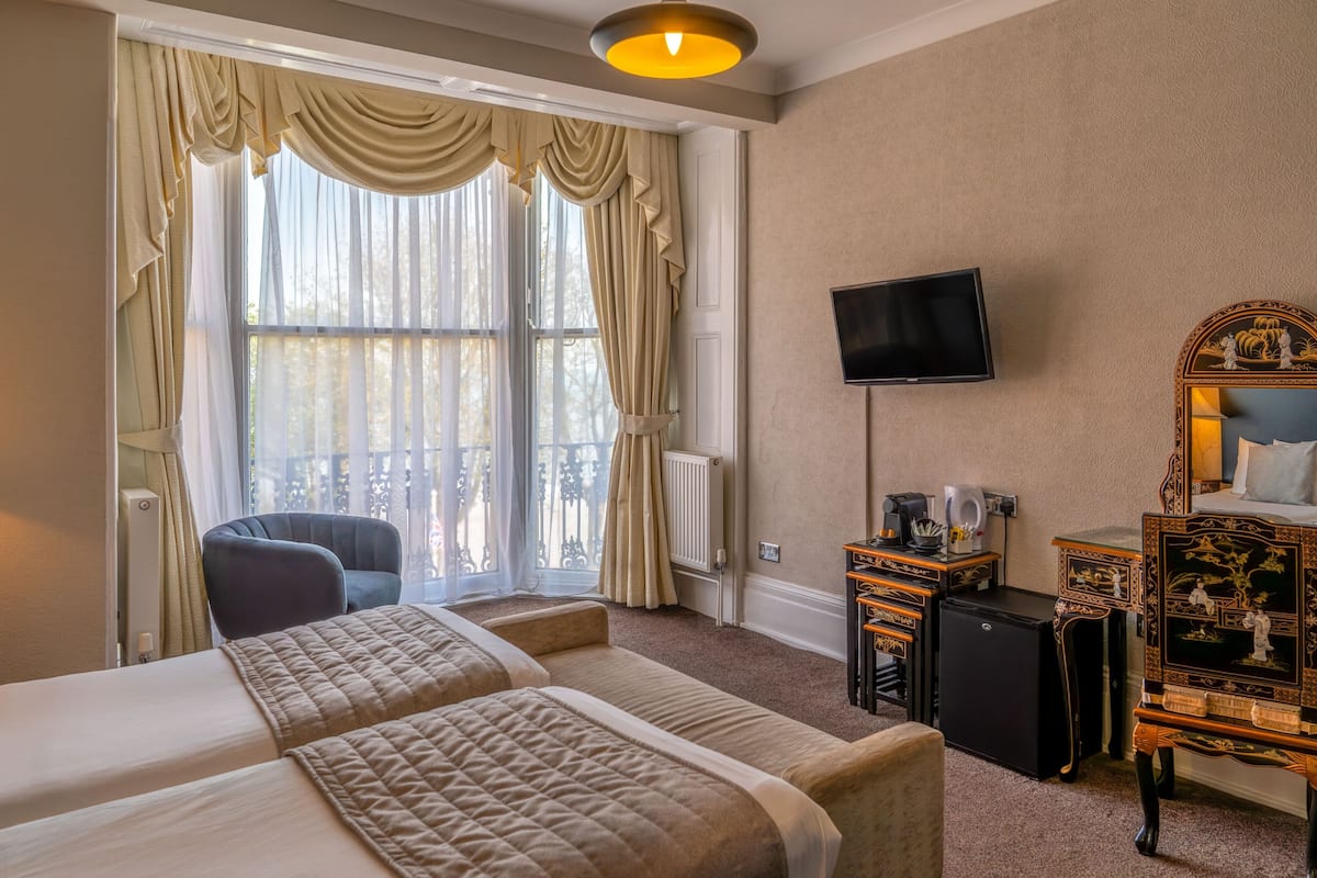 A hotel room with two beds, a TV, a desk, a chair, and a balcony with curtains.
