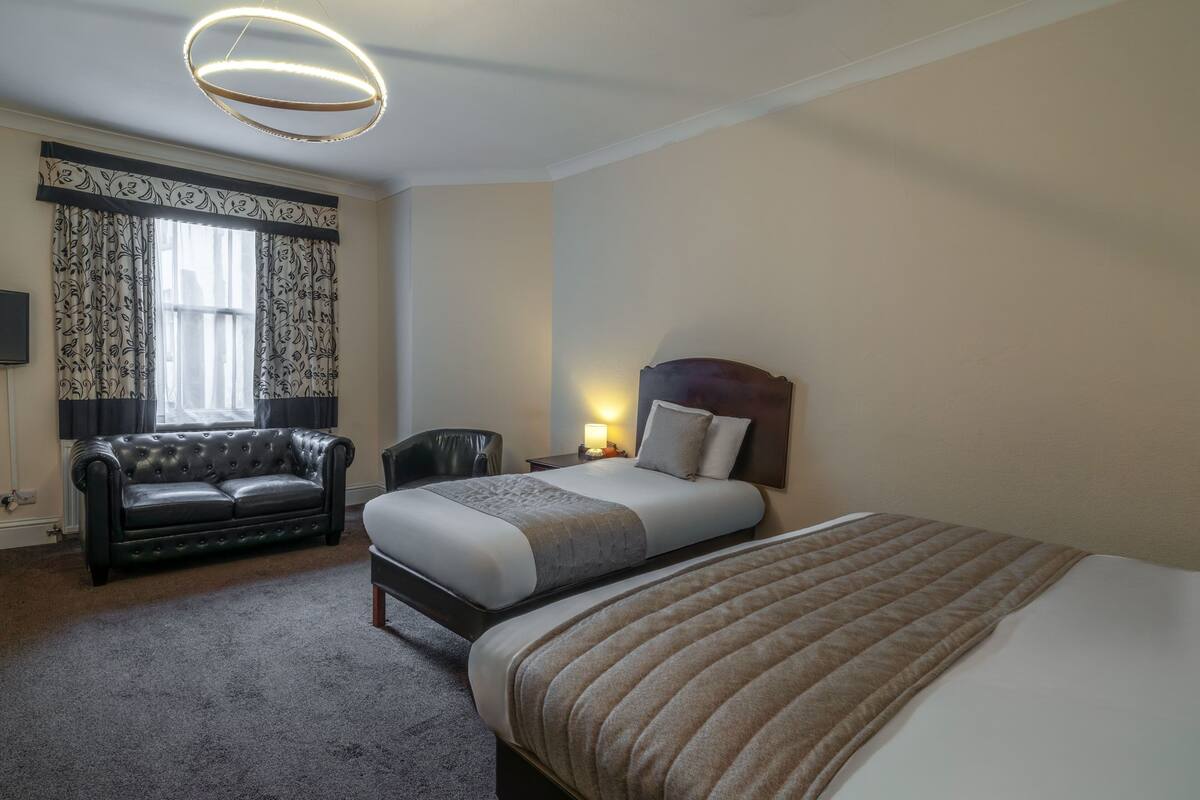 A hotel room with a bed, a sofa, a chair, a nightstand, and a lamp.