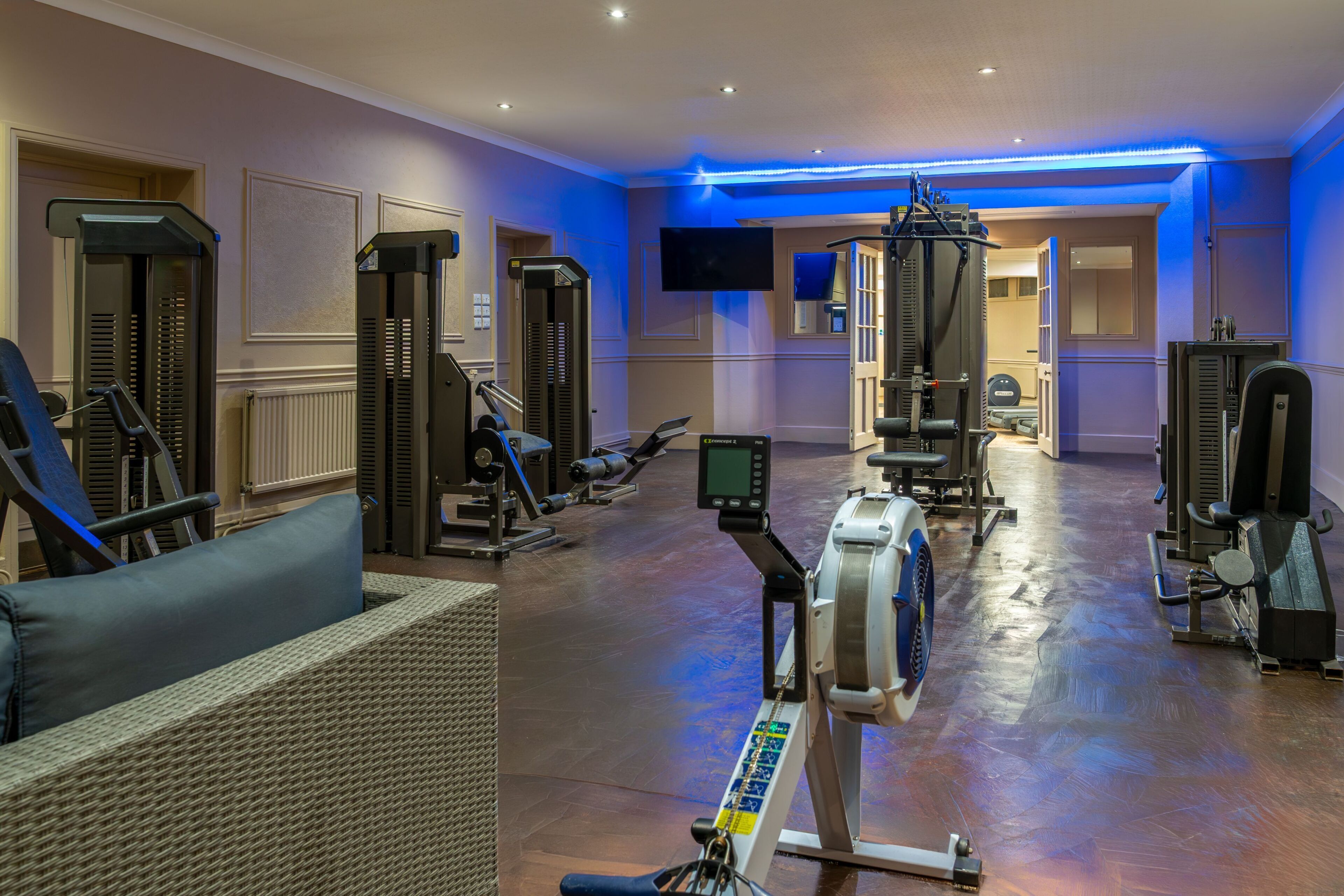 A gym with exercise equipment, a television, and a blue-lit ceiling.