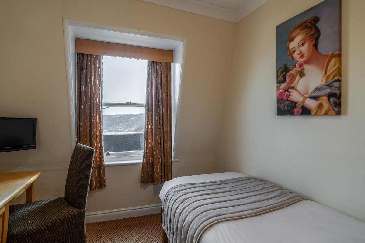 A hotel room with a bed, a chair, a television, and a window with curtains.