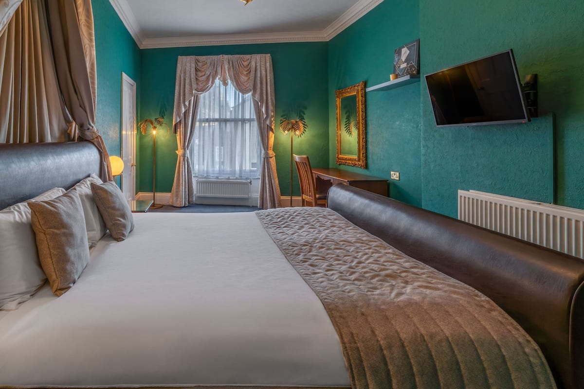 A hotel room with a large bed, a desk, a chair, a television, and a window with curtains.