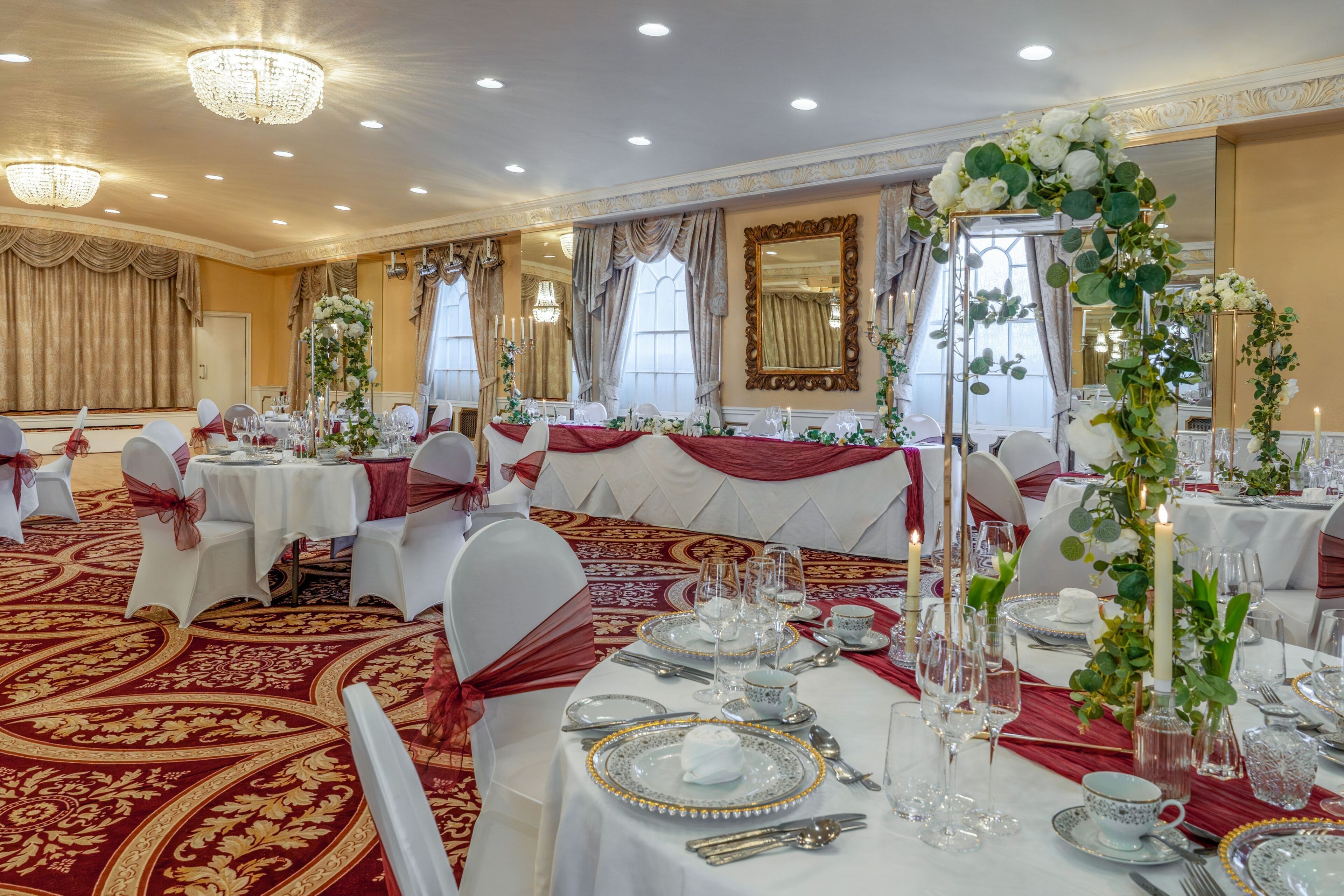 A banquet hall with round tables, chandeliers, and red carpets.