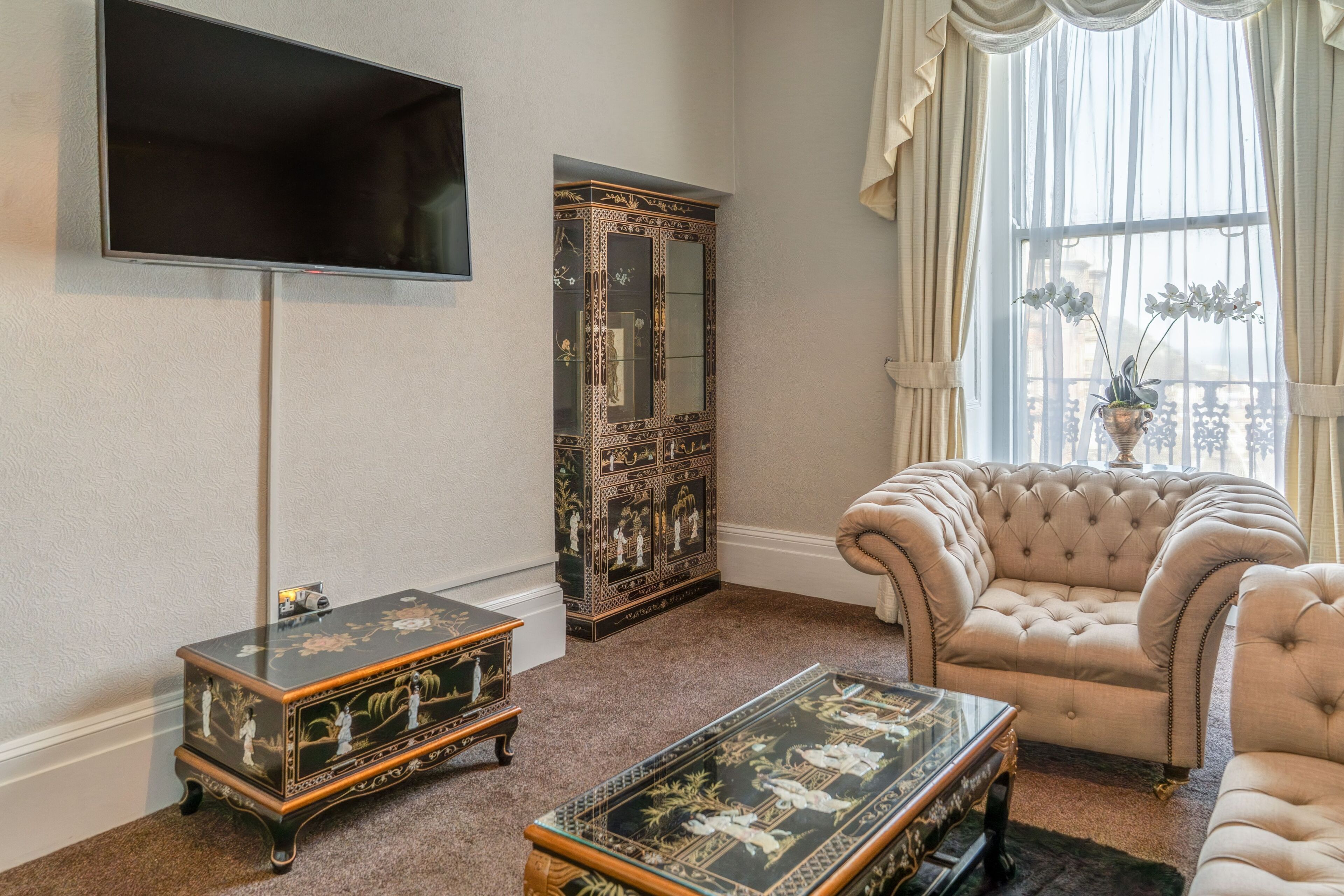 Una sala de estar con televisor de pantalla plana, un aparador decorativo, un sofá capitonado y una mesa de centro.