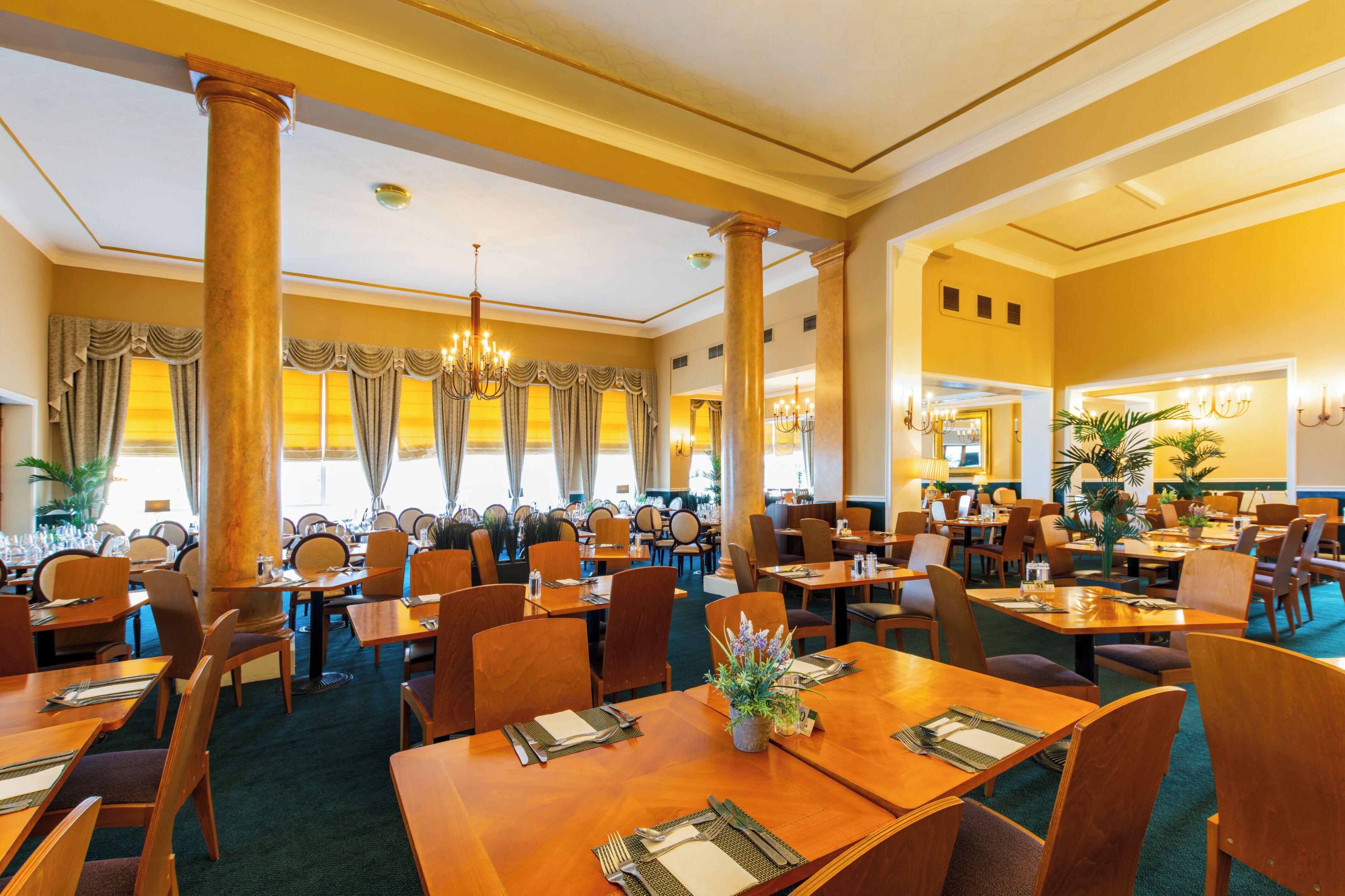 Un restaurant spacieux, doté de nombreuses tables et chaises, de grandes colonnes et de lustres.