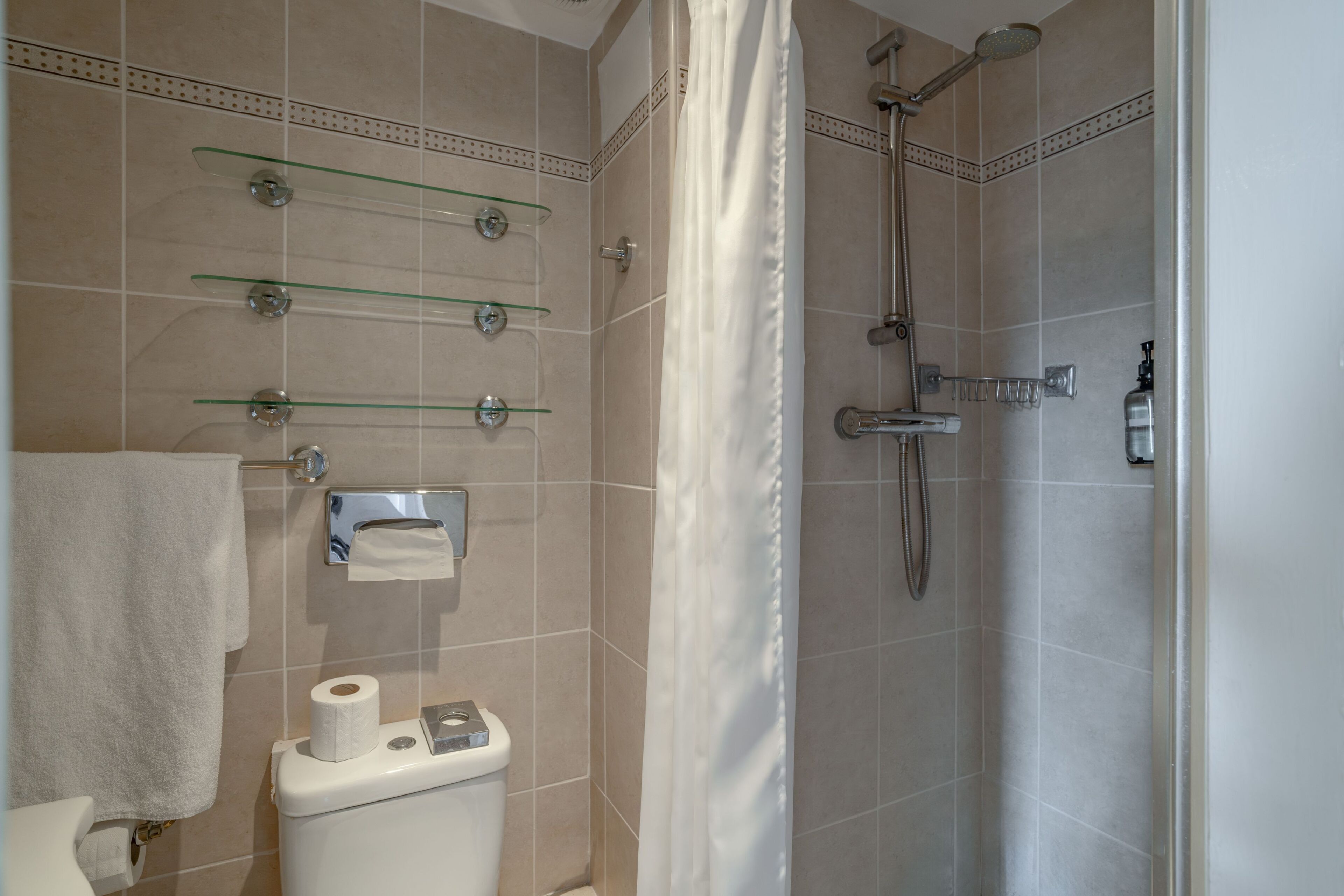 Un baño con inodoro, repisas de vidrio, ducha y perchero.