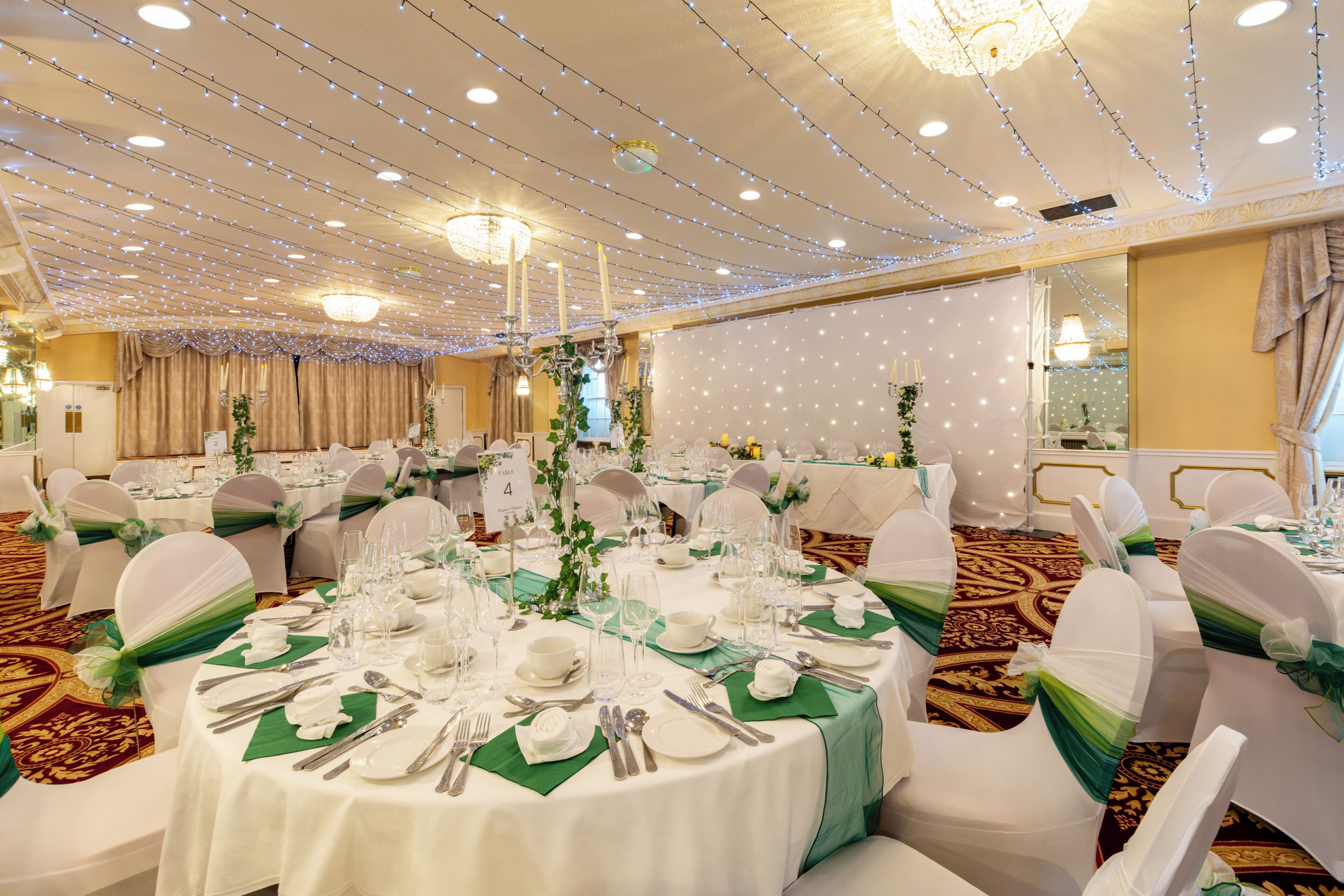 A banquet hall with round tables, white chairs, and string lights.