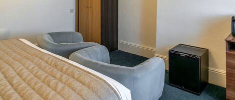 Una habitación de hotel con una cama, dos sillones, un armario, un televisor y un refrigerador pequeño.