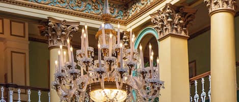 An ornate chandelier with multiple candles, detailed wall carvings, and classical columns.