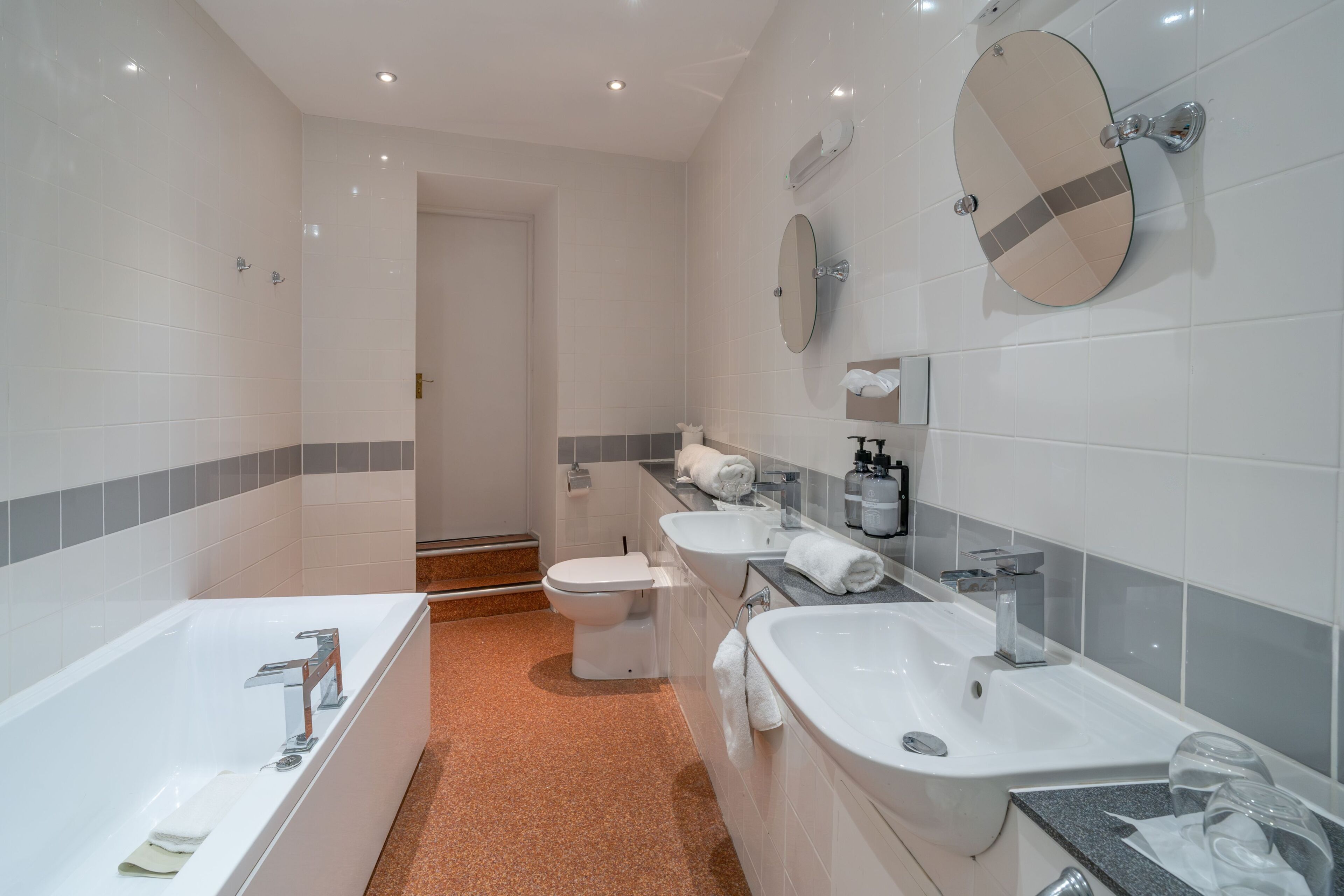 A modern bathroom with a bathtub, two sinks, a toilet, and a shower.
