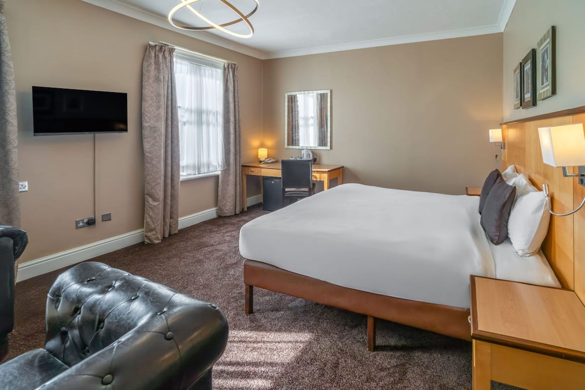 A hotel room with a bed, a desk, a chair, a TV, and a lamp.
