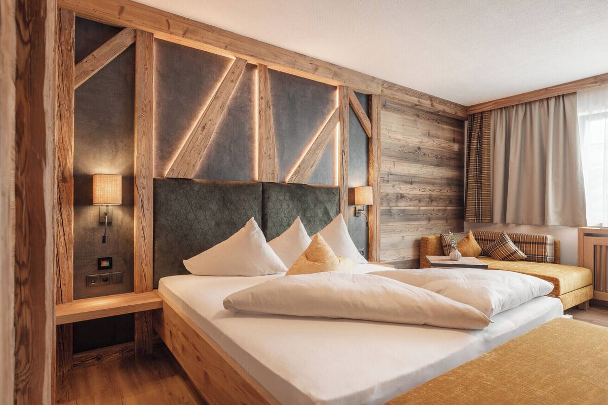 Ein modernes Hotelzimmer mit einem großen Bett, einem Holz-Kopfteil und einer gemütlichen Sitzecke mit Sofa und Beistelltisch.