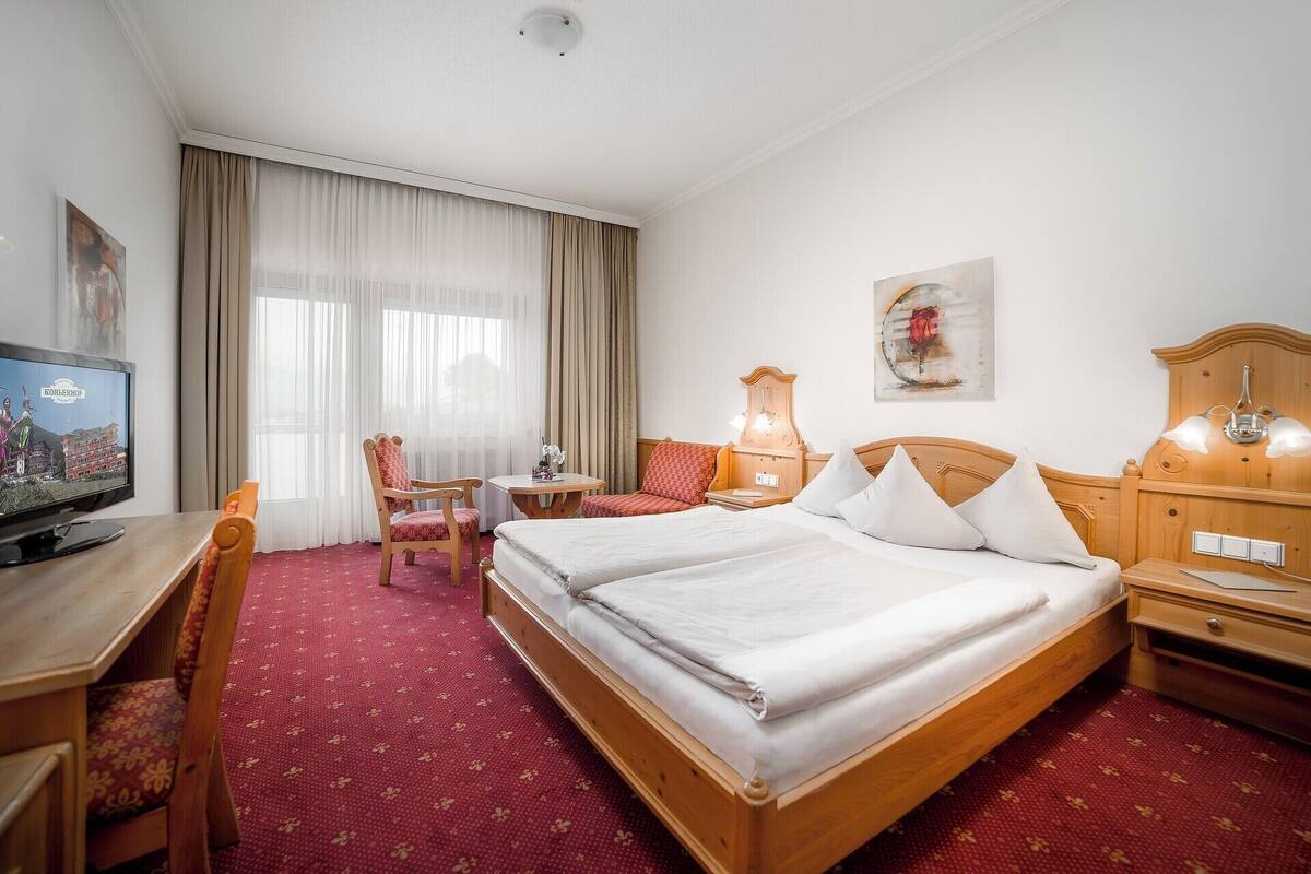 Ein Hotelzimmer mit einem Bett, einem Schreibtisch mit Fernseher, einem Sessel und einem Tisch.